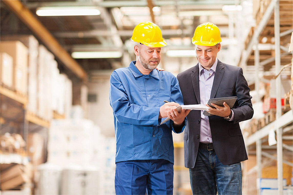 zwei Personen in einer Lagerumgebung mit Blick auf in der Hand liegenden Unterlagen