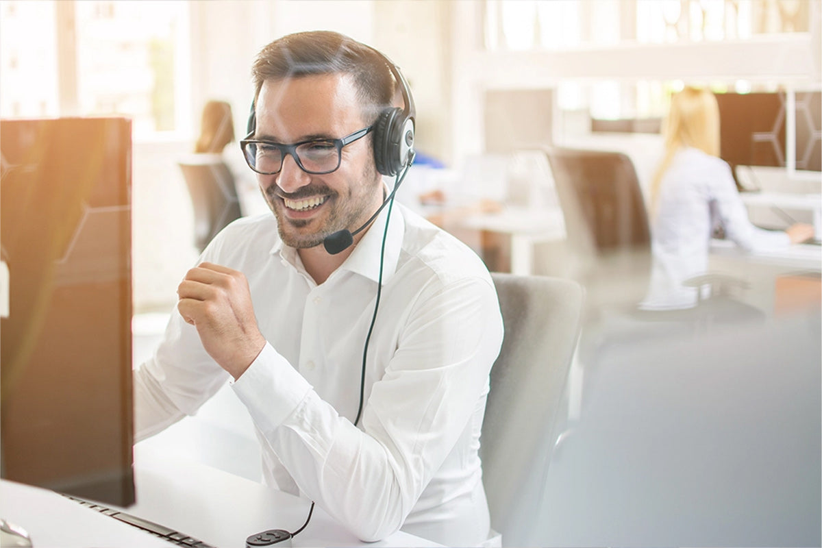 Eine Person in Büroumgebung mit einem Headset und bedient einen PC